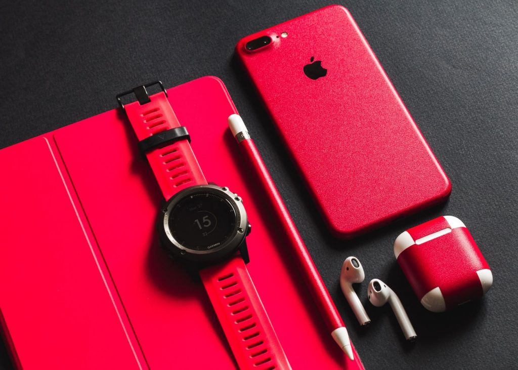 A collection of red electronic devices, including an iPhone, earpods, smartwatch, and more, showcasing a unified and vibrant color scheme.